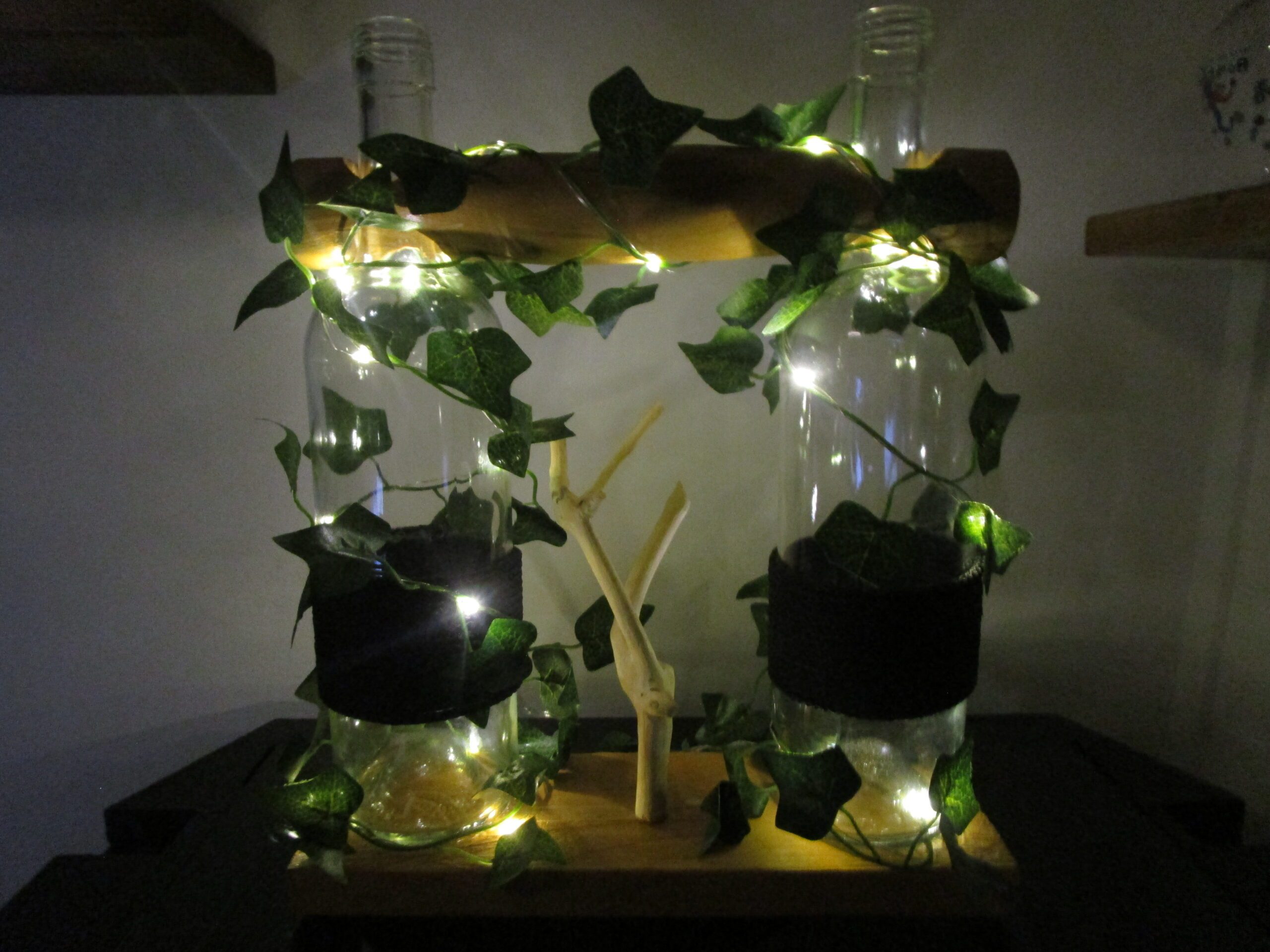 Éclats de récup : Une histoire de lumière et de renaissance Imaginez des objets qui racontent des histoires. "Éclats de récup" est né d'une rencontre entre des objets oubliés et une imagination débordante. Deux bouteilles de verre, autrefois simples contenants, se transforment en piliers d'une création lumineuse. Elles se dressent, témoins d'une métamorphose poétique. Découvrez l'âme du bois. Un morceau de bois, récupéré avec soin, porte les traces de son passé. Poncé et verni, il révèle sa beauté brute et authentique. Il apporte une touche de chaleur et de naturel à l'ensemble, comme un écho de la forêt. Laissez-vous envoûter par la guirlande. Une guirlande de lierre, parsemée de lumières scintillantes, enlace les bouteilles et le bois. Ses feuilles délicates et ses points lumineux créent une atmosphère magique et apaisante. Plongez dans un univers de douceur. La lumière douce et chaleureuse qui émane de la création invite à la rêverie et à la contemplation. Les reflets dans le verre et sur le bois poli ajoutent une dimension féérique à l'ensemble. Admirez un travail artisanal unique. Chaque élément de "Éclats de récup" est choisi et travaillé avec passion. Les bouteilles sont nettoyées et polies, le bois est poncé et verni, et la guirlande est disposée avec délicatesse. Offrez-vous une création éco-responsable. "Éclats de récup" est une invitation à repenser notre rapport aux objets. En valorisant le recyclage et la réutilisation, cette création s'inscrit dans une démarche respectueuse de l'environnement. Invitez la poésie dans votre intérieur. "Éclats de récup" est bien plus qu'un simple objet de décoration. C'est une source d'inspiration, une invitation à ralentir et à apprécier la beauté des choses simples. Adoptez une œuvre qui a une âme. Chaque élément de "Éclats de récup" porte en lui une part de l'histoire de son créateur. En choisissant cette œuvre, vous vous offrez un morceau d'authenticité et de poésie.