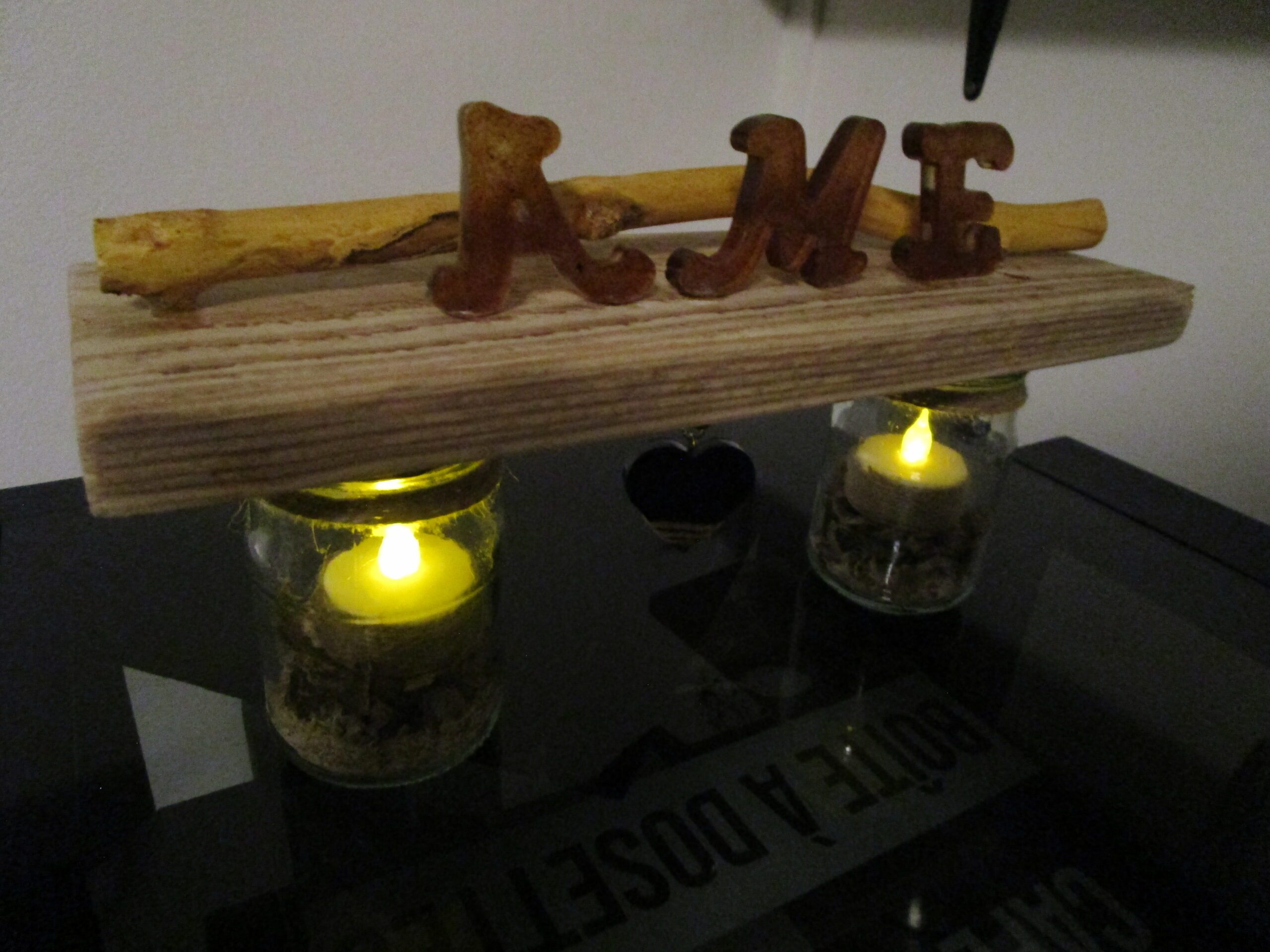 "Apportez une touche d'originalité à votre décoration avec ce luminaire DIY. Deux bocaux en verre, transformés en bougeoirs, sont reliés par une structure en bois brut. Des lettres en bois, formant le mot "AME", apportent une touche décorative et personnalisée. Un cœur en bois suspendu complète cette création unique."