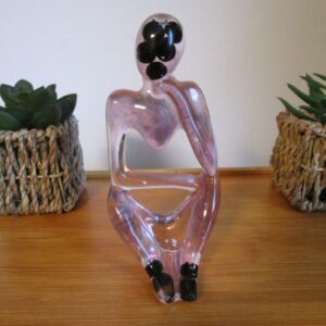 L'Éveil de la Conscience. En explorant la sculpture, vous sentez la douceur de la résine, légèrement fraîche au toucher. Quelques petites irrégularités attirent votre attention : ce sont les perles de tourmaline, incrustées dans la matière. Elles sont plus dures et plus froides que la résine, offrant une texture contrastée. La forme de la sculpture évoque une personne assise, en pleine réflexion. Vous pouvez sentir la position des jambes repliées, la courbe du torse et la forme de la tête. C'est une invitation à imaginer la posture du penseur, absorbé dans ses pensées.