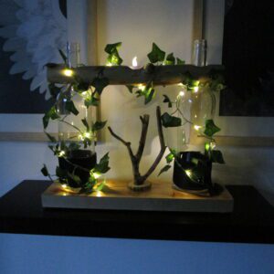 Bois Lumineux : création artisanale, bouteilles recyclées, branches naturelles, lierre lumineux. Un éclat de nature pour votre intérieur. "Deux bouteilles de verre, autrefois destinées à être jetées, se transforment en luminaires poétiques. Une guirlande lumineuse telle une liane scintillante, enlace les bouteilles, parée de feuilles artificielles. Au centre, une structure en bois brut, tel un totem lumineux, complète cette scène enchantée. Une création qui célèbre la beauté du recyclage et la magie de la lumière."