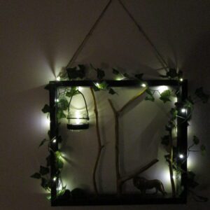 Nuit de Safari, une décoration qui apporte exotisme et sérénité. Artisanat et nature sauvage. Un carré de nuit boisée, où des branches cherchent le ciel. Une lueur captive danse dans un verre suspendu. Des étoiles filantes de lumière enlacent le tout. Un lion, gardien silencieux, veille sur ce monde miniature.
