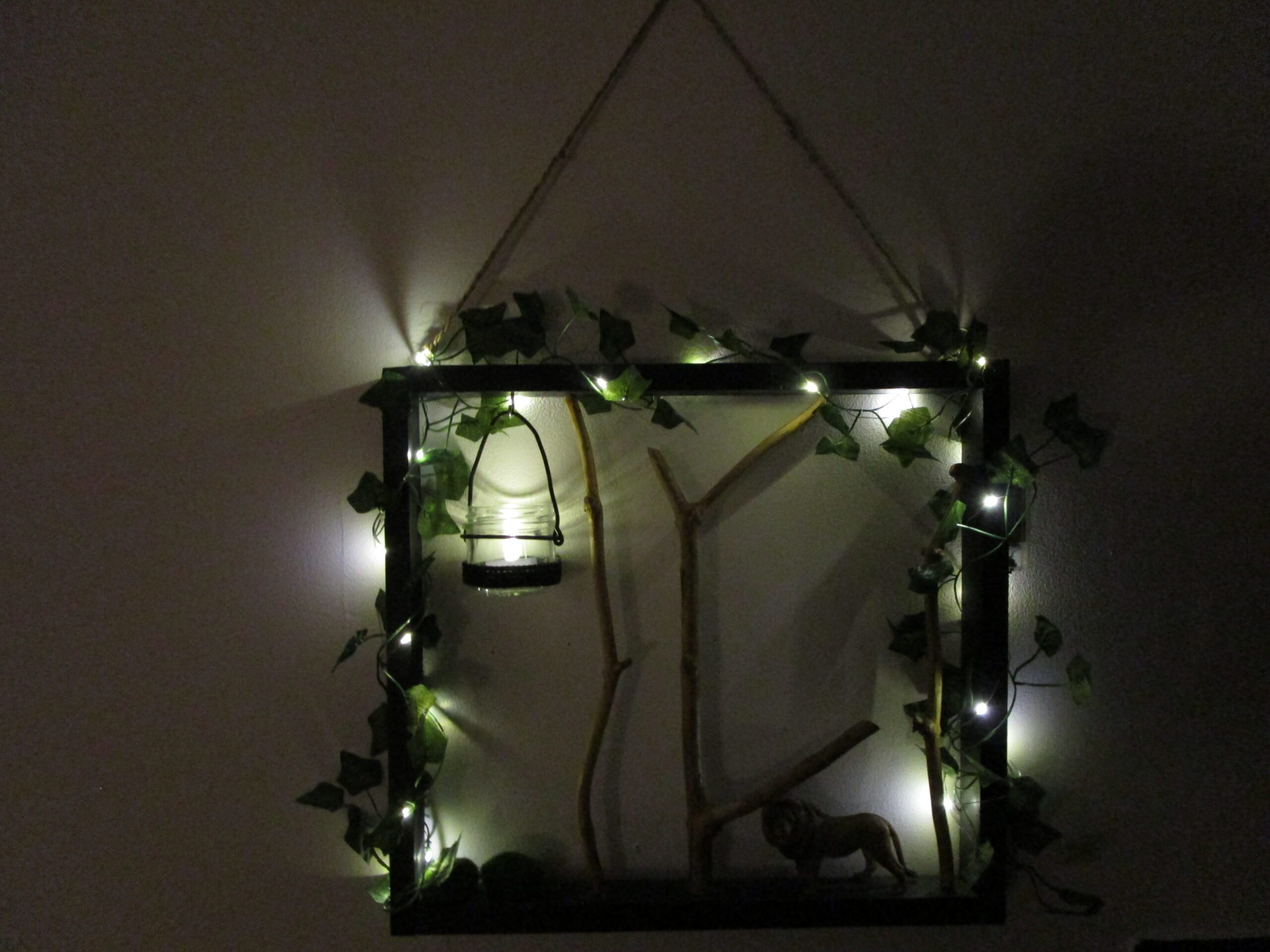 Nuit de Safari, une décoration qui apporte exotisme et sérénité. Artisanat et nature sauvage. Un carré de nuit boisée, où des branches cherchent le ciel. Une lueur captive danse dans un verre suspendu. Des étoiles filantes de lumière enlacent le tout. Un lion, gardien silencieux, veille sur ce monde miniature.