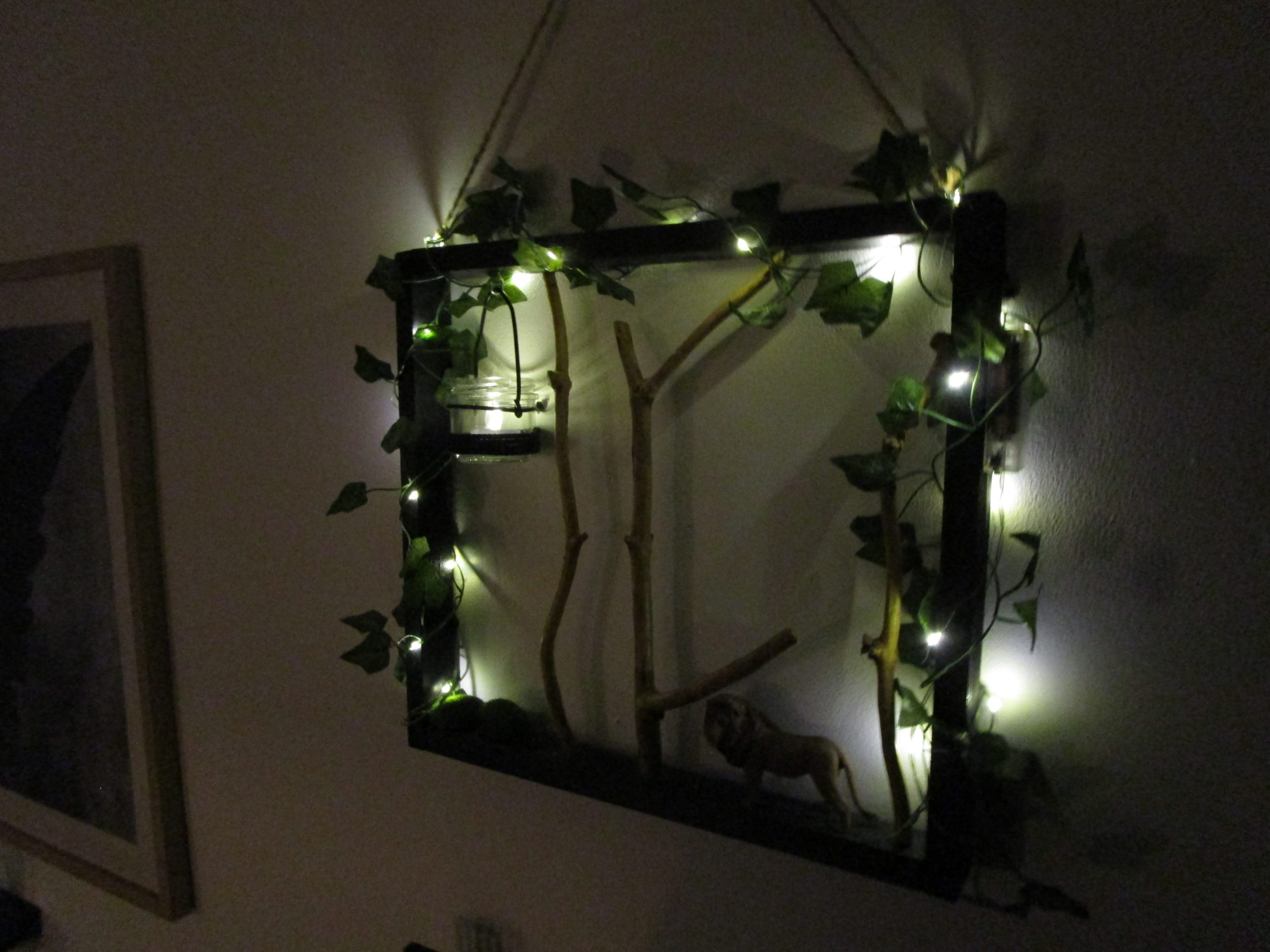 Un carré de nuit boisée, où des branches cherchent le ciel. Une lueur captive danse dans un verre suspendu. Des étoiles filantes de lumière enlacent le tout. Un lion, gardien silencieux, veille sur ce monde miniature.