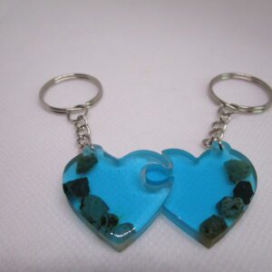 Duo de porte-clés "Cœurs de Lagon" artisanaux. Chaque porte-clé est un demi-cœur en résine turquoise transparente, incrusté de pierres brutes. Les deux moitiés s'assemblent pour former un cœur complet.