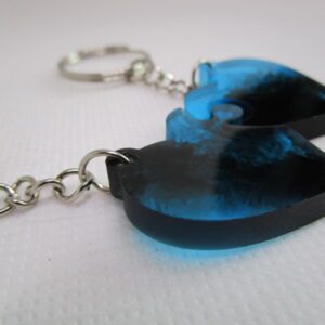 Duo de porte-clés "Cœurs le Grand Bleu" artisanaux. Chaque porte-clé est un demi-cœur en résine bleue et transparente, avec des nuances de bleu évoquant l'océan. Les deux moitiés s'assemblent pour former un cœur complet.