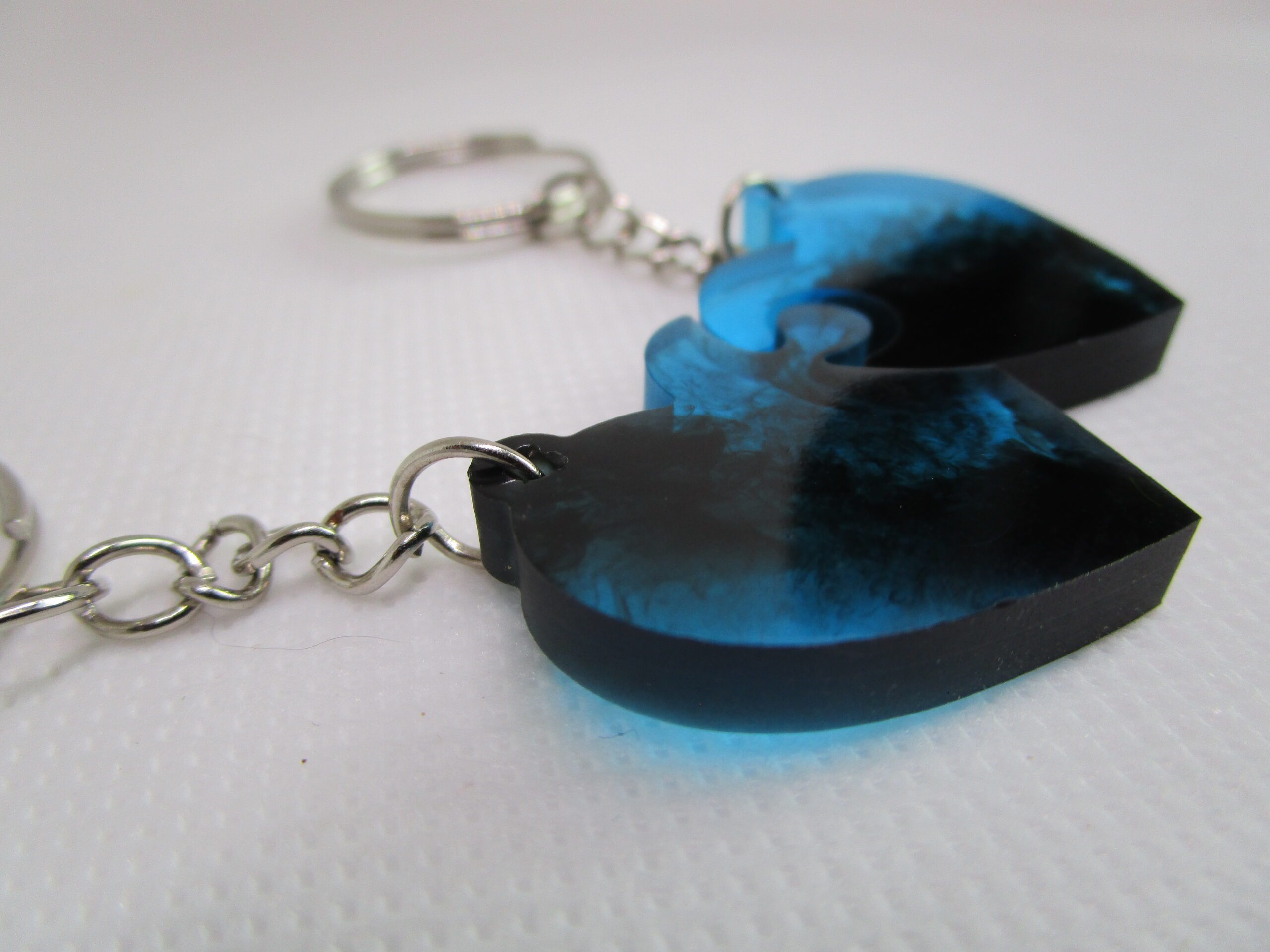 Duo de porte-clés "Cœurs le Grand Bleu" artisanaux. Chaque porte-clé est un demi-cœur en résine bleue et transparente, avec des nuances de bleu évoquant l'océan. Les deux moitiés s'assemblent pour former un cœur complet.