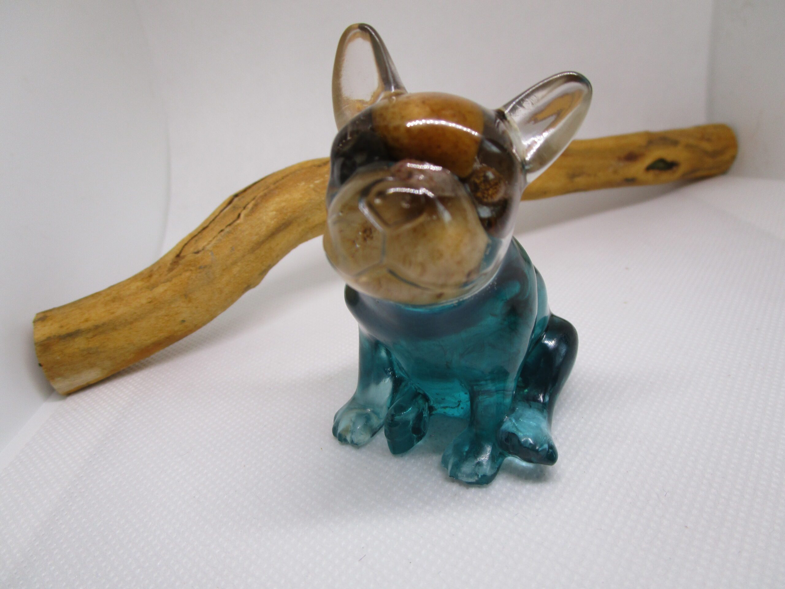 Bouledogue Méditerranéen : Un Rayon de Soleil Artisanal Apportez une touche de chaleur méditerranéenne à votre intérieur avec notre sculpture "Bouledogue Méditerranéen". Cette pièce unique, façonnée à la main, est une véritable célébration de la beauté des paysages côtiers. Elle associe la clarté de la résine bleu turquoise aux nuances profondes du noir et à la beauté brute des pierres naturelles. Un Design Inspiré des Paysages Méditerranéens Chaque pierre est un fragment de la côte, un souvenir de plages ensoleillées et de criques cachées. La résine bleu turquoise évoque la clarté des eaux cristallines, tandis que le noir ajoute une dimension de profondeur et de mystère. La silhouette du bouledogue, avec son expression amicale et sa posture robuste, apporte une touche de charme et de caractère. Une Lumière Douce et Chaleureuse, Créant une Ambiance Conviviale La lumière naturelle révèle les nuances de la résine, les textures des pierres et les détails de la sculpture, créant un spectacle visuel captivant. Elle invite à la détente et à la convivialité, transformant votre espace en un havre de paix méditerranéen. Cette sculpture est idéale pour créer une ambiance chaleureuse et accueillante. Un Objet Décoratif Unique et Authentique, Reflet de l'Artisanat Local "Bouledogue Méditerranéen" est bien plus qu'une simple sculpture. C'est une œuvre d'art qui témoigne d'un savoir-faire artisanal et d'un amour pour les paysages méditerranéens. Son design unique et ses matériaux naturels en font un objet décoratif qui ne manquera pas de susciter l'admiration. Caractéristiques Matériaux : Résine bleu turquoise, résine noire, pierres naturelles Fabrication : Artisanale, chaque pièce est unique Design : Inspiré des paysages méditerranéens, s'adapte à tous les styles d'intérieur Lumière : Douce et chaleureuse, crée une ambiance conviviale Conseils d'Entretien Pour préserver la beauté de votre sculpture, nous vous recommandons de la nettoyer délicatement avec un chiffon doux. Évitez l'exposition prolongée au soleil et aux sources de chaleur intense. Apportez un rayon de soleil méditerranéen à votre intérieur avec "Bouledogue Méditerranéen". Cette sculpture est une invitation à la détente et à la convivialité, un véritable hommage à la beauté des paysages côtiers.
