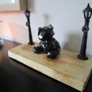 Le Gardien de la Lumière un ourson en résine scintillant, niché sur un socle en bois chaleureux, et mis en valeur par deux lampadaires miniatures. Cette pièce unique apportera une touche de magie et de douceur à votre intérieur.