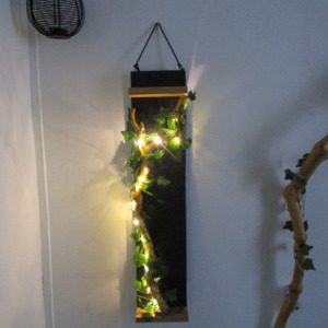 "Découvrez cette création murale unique, un mariage subtil de design moderne et de touches naturelles. Une structure rectangulaire épurée, soulignée par des finitions en bois clair, sert de support à une guirlande lumineuse LED. Celle-ci, enlacée de feuilles artificielles, crée un contraste saisissant entre la sophistication de la forme et la douceur organique de la végétation. Cette pièce apportera une touche de lumière et de verdure à votre intérieur, tout en conservant une esthétique minimaliste et contemporaine."