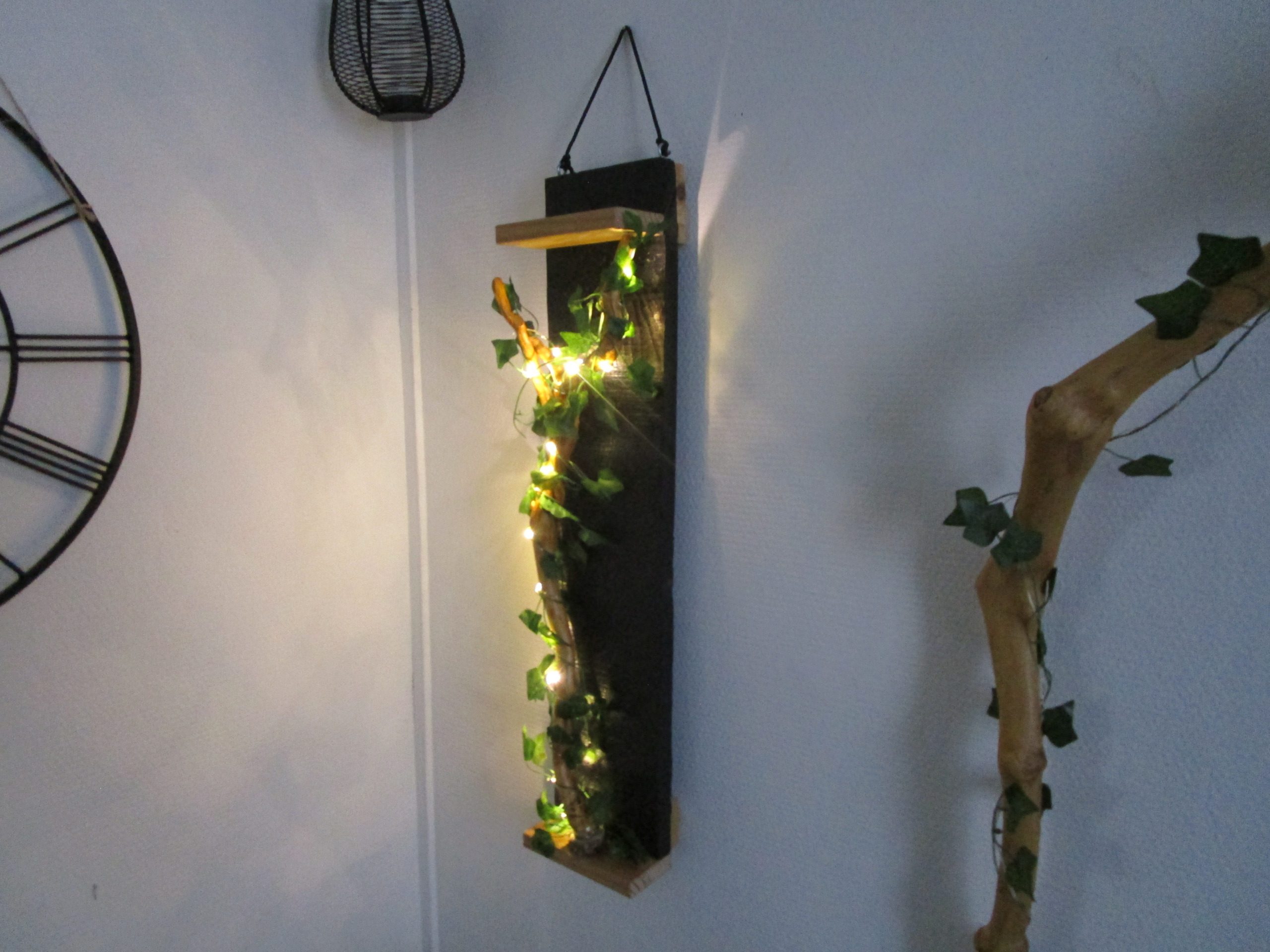 "Découvrez cette création murale unique, un mariage subtil de design moderne et de touches naturelles. Une structure rectangulaire épurée, soulignée par des finitions en bois clair, sert de support à une guirlande lumineuse LED. Celle-ci, enlacée de feuilles artificielles, crée un contraste saisissant entre la sophistication de la forme et la douceur organique de la végétation. Cette pièce apportera une touche de lumière et de verdure à votre intérieur, tout en conservant une esthétique minimaliste et contemporaine."