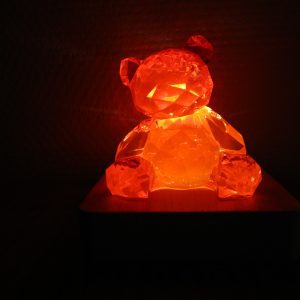 Posé sur son socle en bois forme carré, tel un joyau sur un coussin, l’ourson Ruby Light fait en résine rouge transparente règne sur son petit monde de lumière. Il est l’incarnation de la beauté, de la magie et de l’éclat éternel.