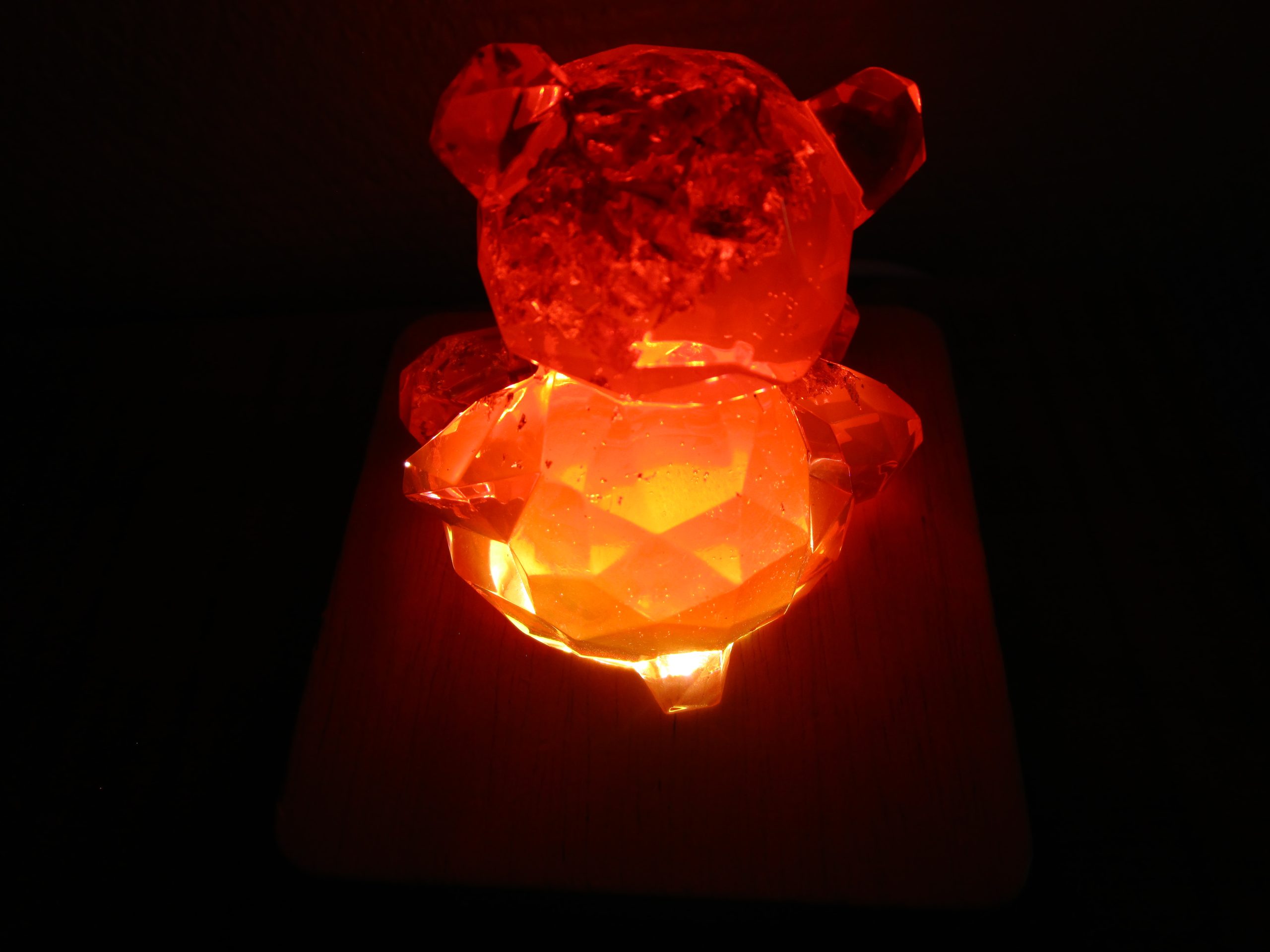 Posé sur son socle en bois forme carré, tel un joyau sur un coussin, l’ourson fait en résine rouge transparente règne sur son petit monde de lumière. Il est l’incarnation de la beauté, de la magie et de l’éclat éternel.