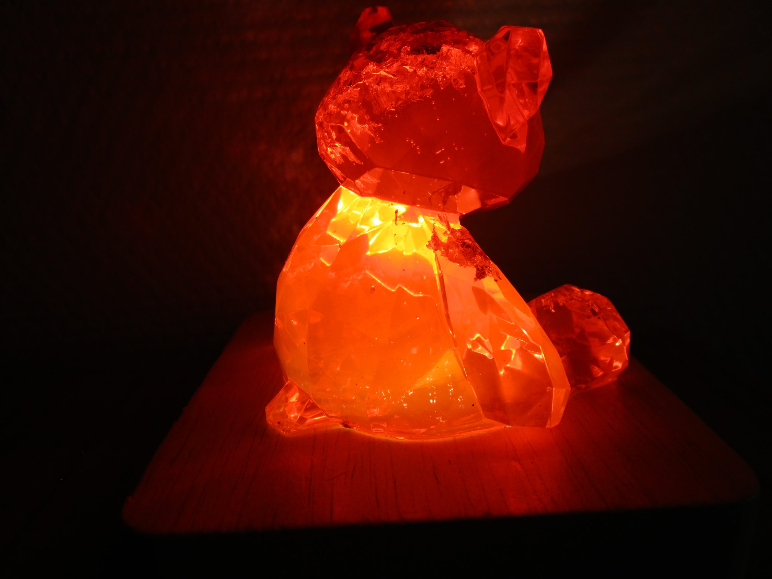 Posé sur son socle en bois forme carré, tel un joyau sur un coussin, l’ourson fait en résine rouge transparente règne sur son petit monde de lumière. Il est l’incarnation de la beauté, de la magie et de l’éclat éternel.