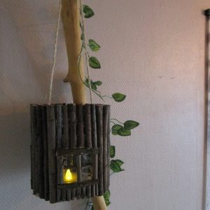 Le refuge du lutin laissez la magie de la forêt s'inviter chez vous avec cette lanterne unique. "Imaginez une petite maison, , conçue comme une lanterne. La base est un cylindre de verre lisse et frais, comme un pot de confiture. Tout autour, des dizaines de petits bâtonnets de bois, rugueux et irréguliers, sont collés côte à côte. Ils forment une surface texturée, comme l'écorce d'un arbre. À l'avant, une ouverture rectangulaire laisse entrevoir une lumière douce et chaude. Une petite flamme artificielle qui diffuse une lumière constante.