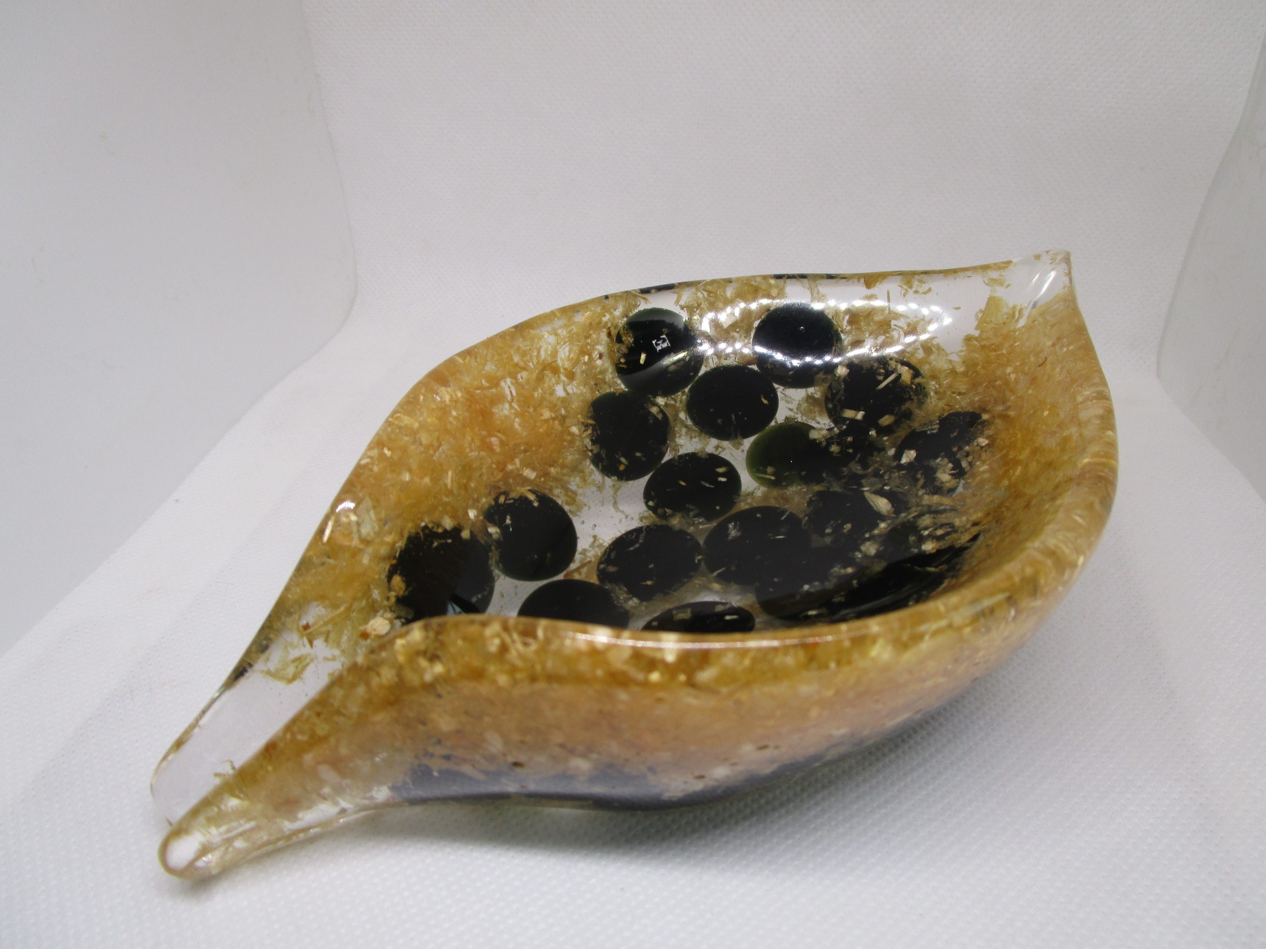 Éclats d'Obsidienne Dorée "Image d'une création artisanale en forme de feuille, réalisée en résine transparente avec des inclusions de copeaux de bois dorés et des pierres plates noires d'obsidienne, vue en perspective sur un fond clair."
