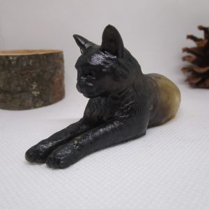 "Image d'un chat en résine noire, en position couchée, avec des morceaux de bois clair incrustés dans la résine. L'œuvre est intitulée 'Protecteur des Bois'."