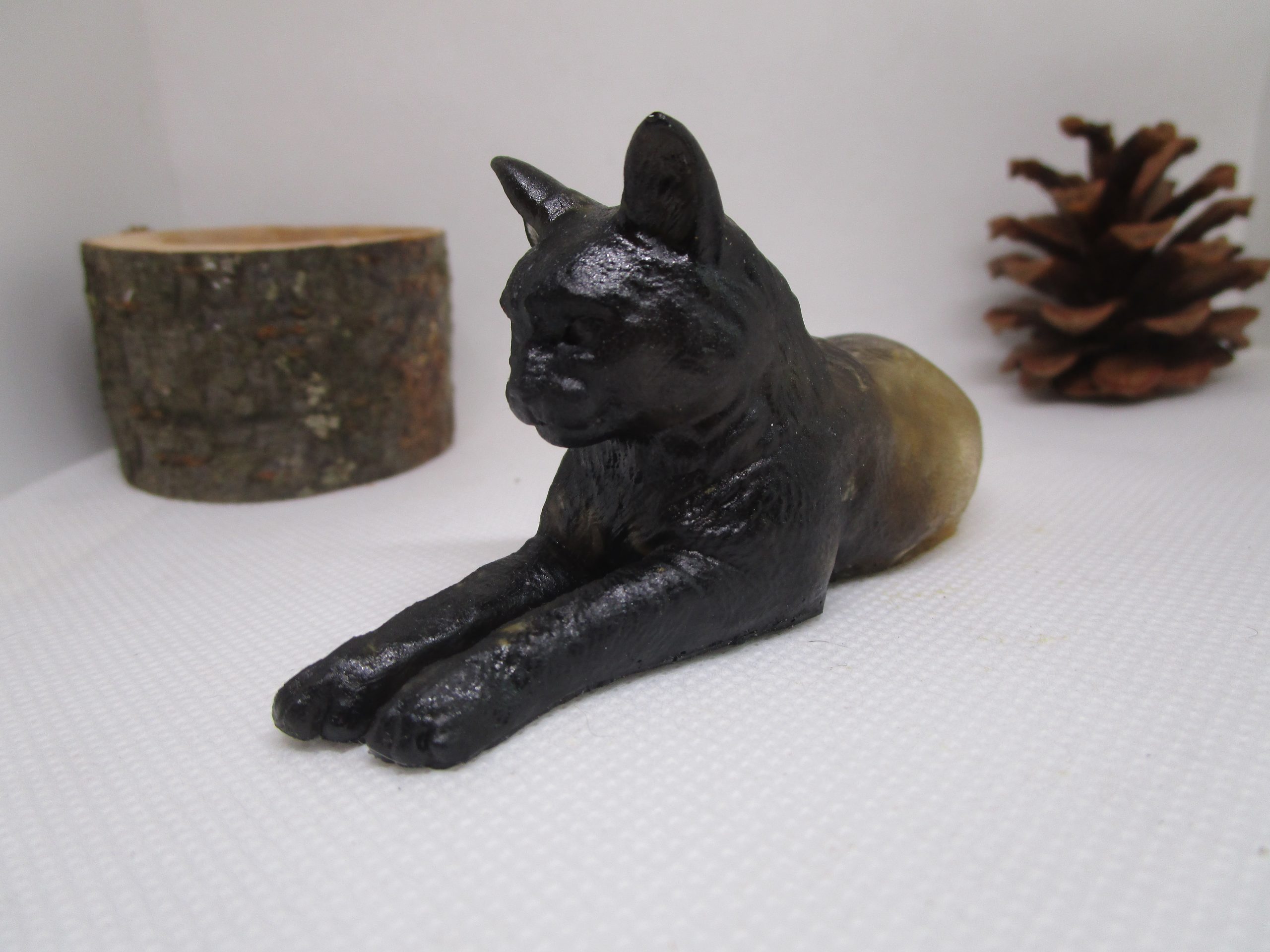 "Image d'un chat en résine noire, en position couchée, avec des morceaux de bois clair incrustés dans la résine. L'œuvre est intitulée 'Protecteur des Bois'."