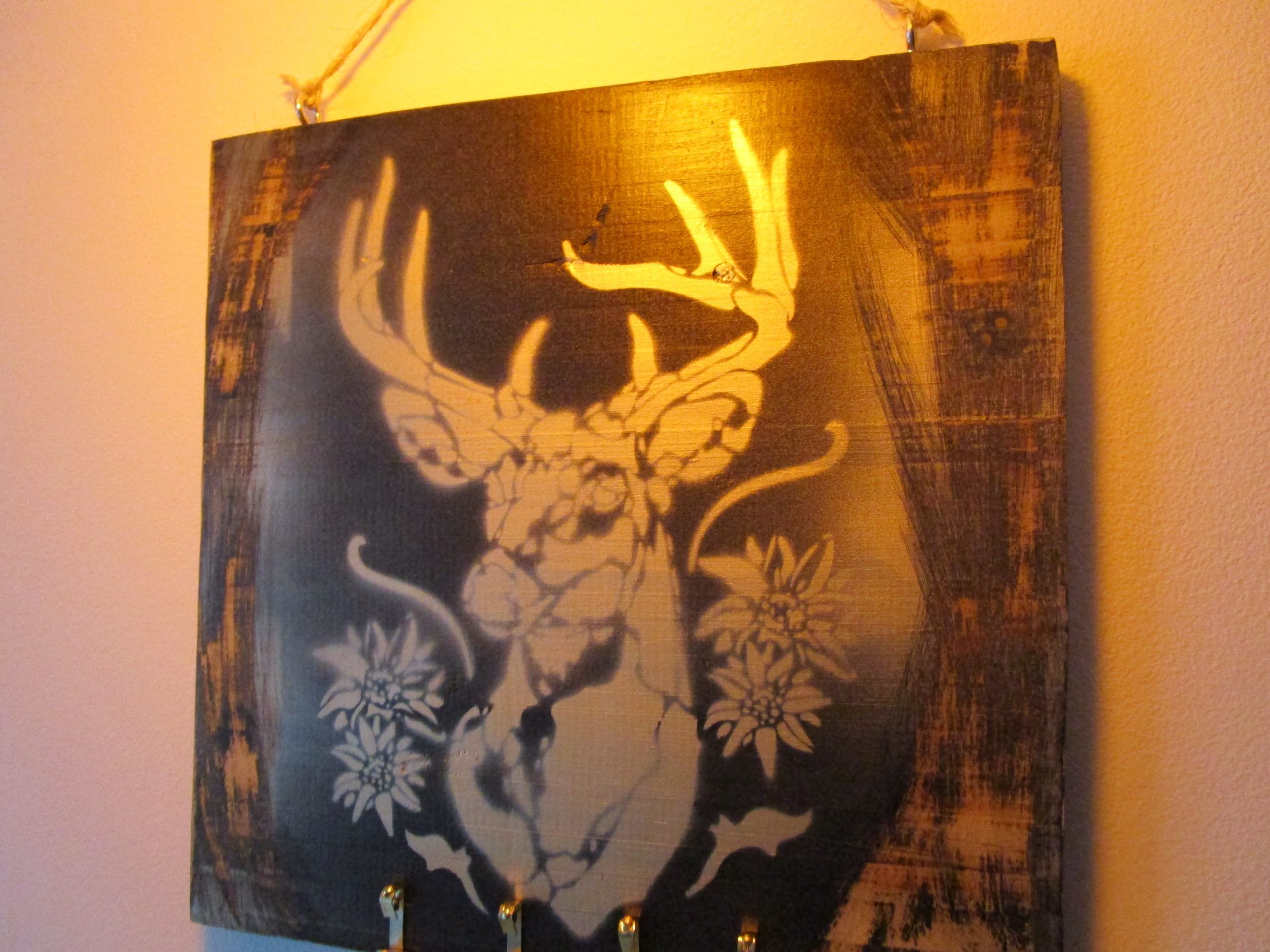 L'Esprit des Alpes "Tableau en bois recyclé, cerf peint à la bombe, touches alpines, crochets pour clés. L'empreinte de l'artiste signe cette pièce unique, où nature et fonctionnalité s'enlacent."