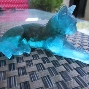 Chat des Forêts Figurine artisanale représentant un chat couché, en résine bleu clair avec des incrustations de mousse naturelle verte.