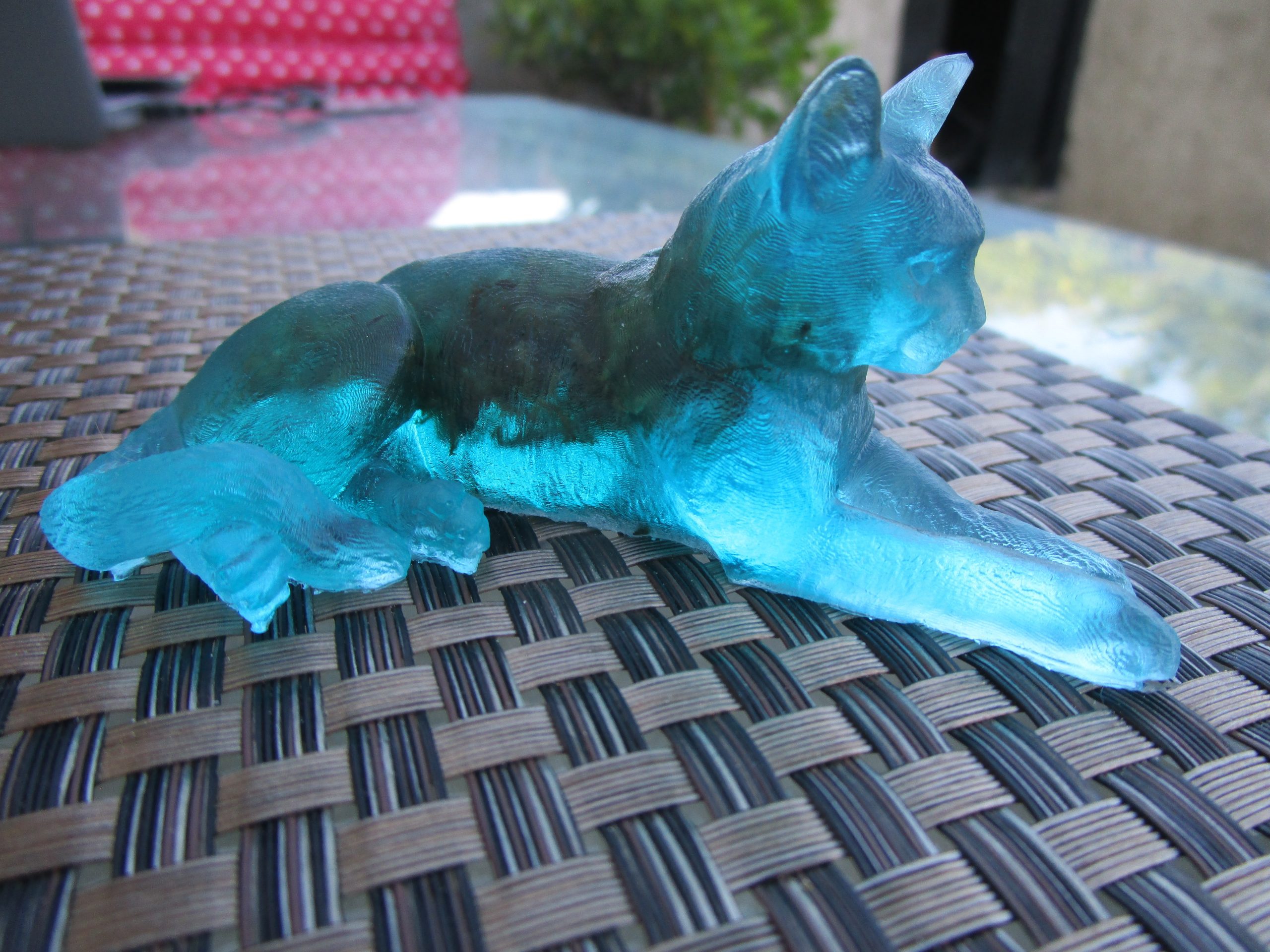 Chat des Forêts Figurine artisanale représentant un chat couché, en résine bleu clair avec des incrustations de mousse naturelle verte.