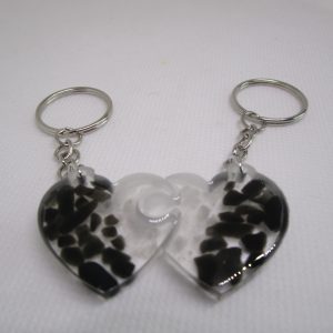 L'Âme Sœur Minérale Porte-clés artisanaux représentant deux demi-cœurs en résine claire contenant des morceaux de cristal de roche (blanc) et d'obsidienne noire.