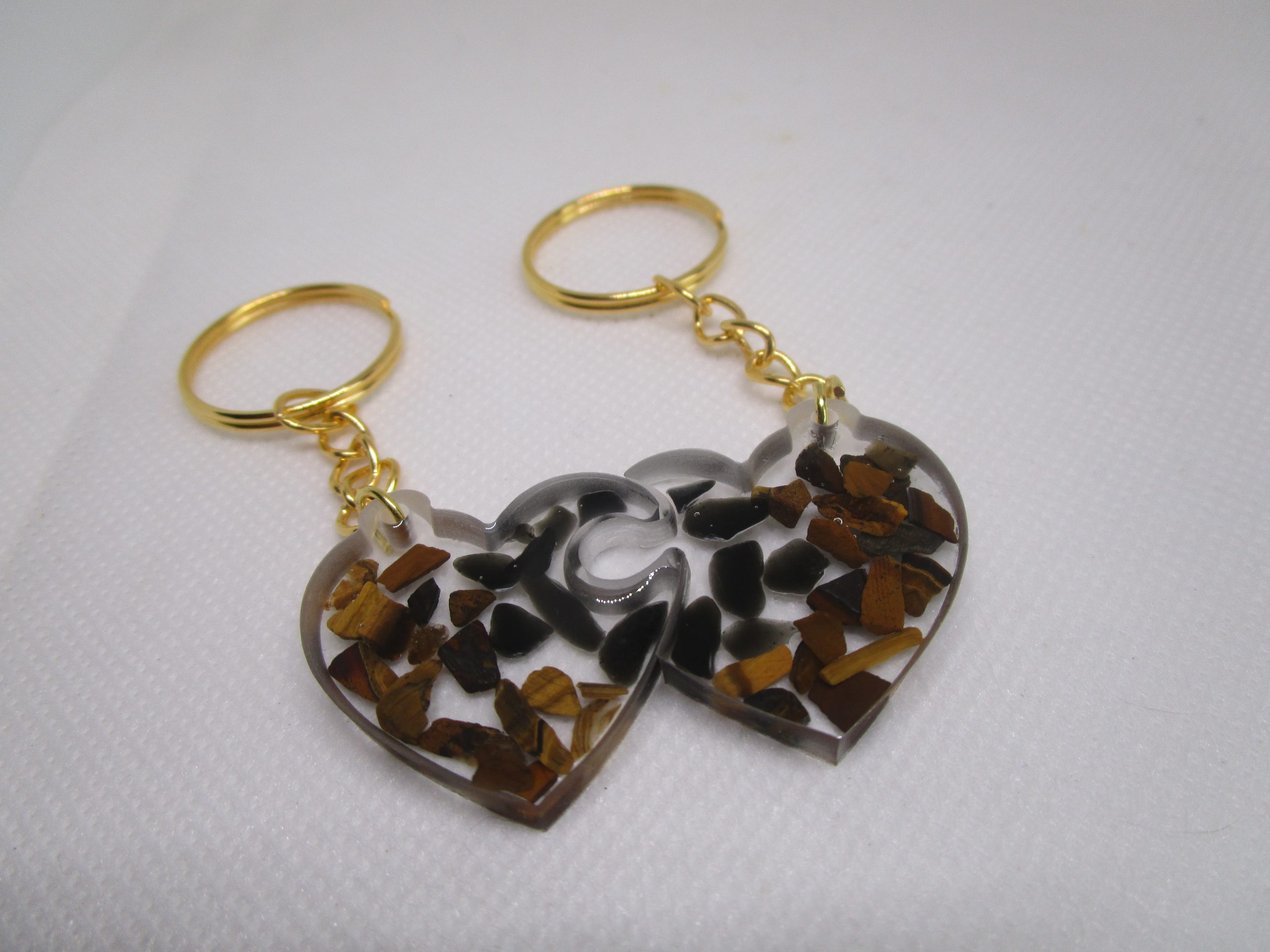 Amour Protégé. Porte-clés artisanaux en résine transparente avec des éclats d'obsidienne noire et d'œil de tigre dorée, formant un cœur.