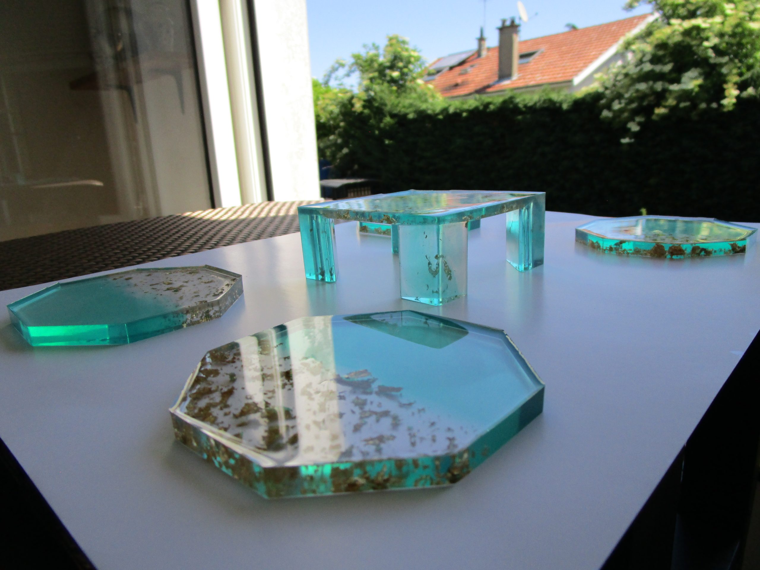 Boréal Doré "Service de dessous de verre 'Boréal Doré' fait main en résine vert turquoise et transparente avec incrustations de feuilles d'or, présenté avec son socle assorti."