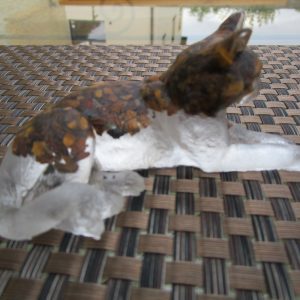 "Sculpture de chat couchée en résine transparente, incrustée de pierres naturelles œil de tigre. La partie supérieure du corps du chat est marbrée de couleurs terreuses et dorées dues aux pierres."