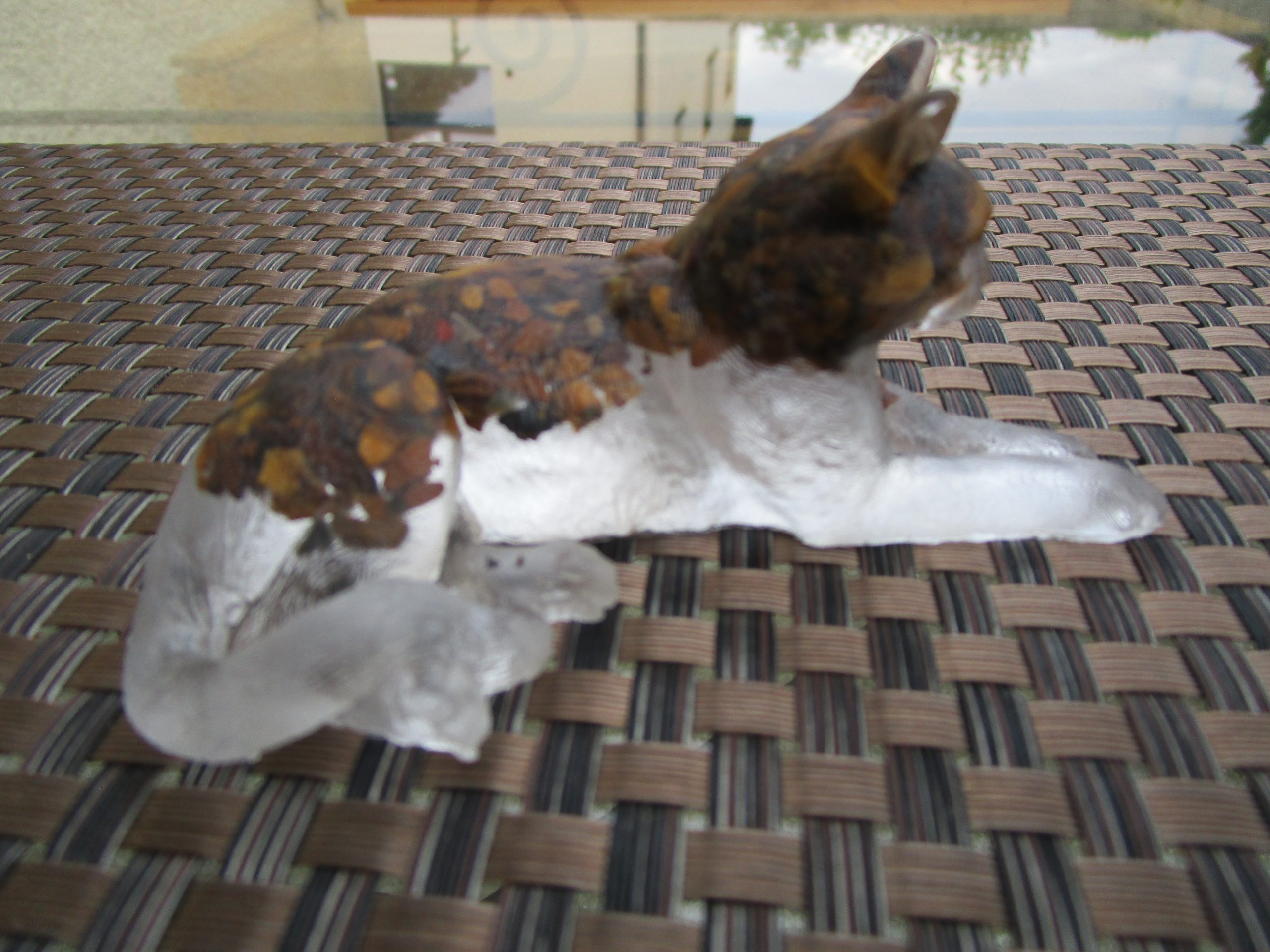 "Sculpture de chat couchée en résine transparente, incrustée de pierres naturelles œil de tigre. La partie supérieure du corps du chat est marbrée de couleurs terreuses et dorées dues aux pierres."