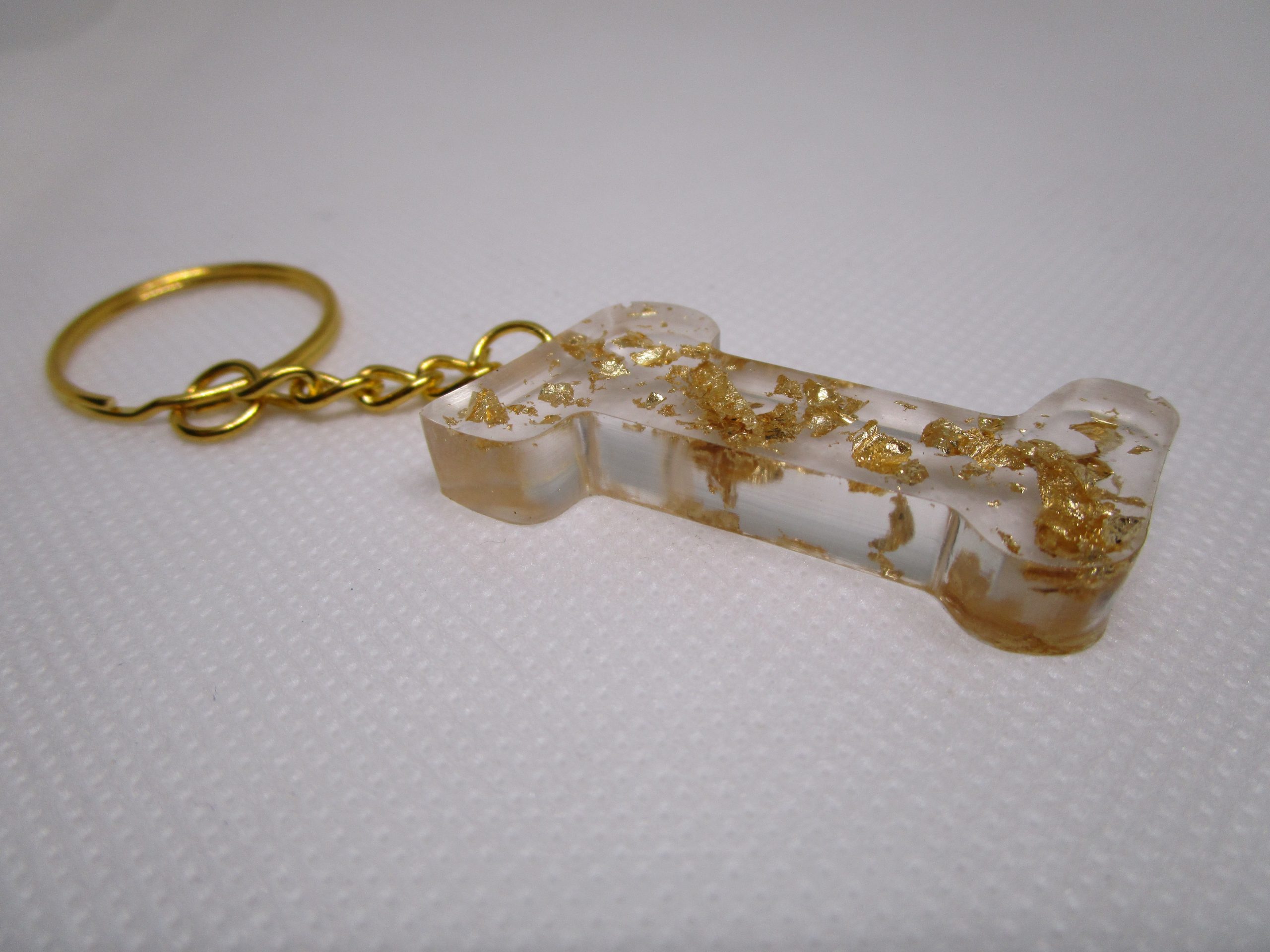 Porte-clés en résine transparente en forme de I, incrusté de feuilles d'or, avec un anneau doré et une chaîne.