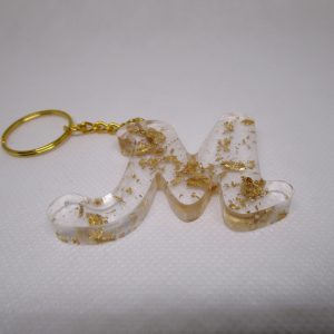 Porte-clés en résine transparente en forme de lettre "M", incrusté de feuilles d'or, avec un anneau doré et une chaîne.
