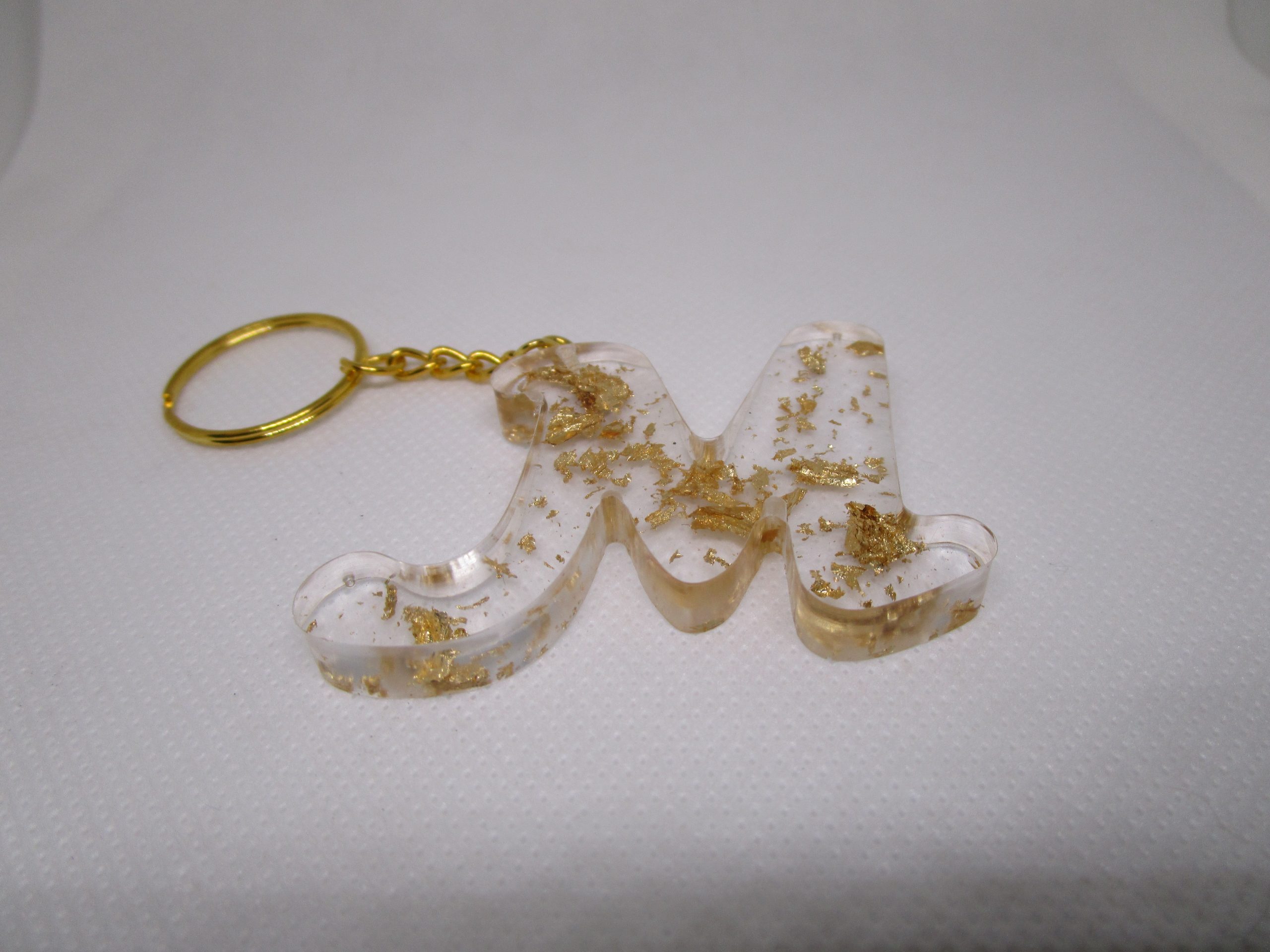Porte-clés en résine transparente en forme de lettre "M", incrusté de feuilles d'or, avec un anneau doré et une chaîne.