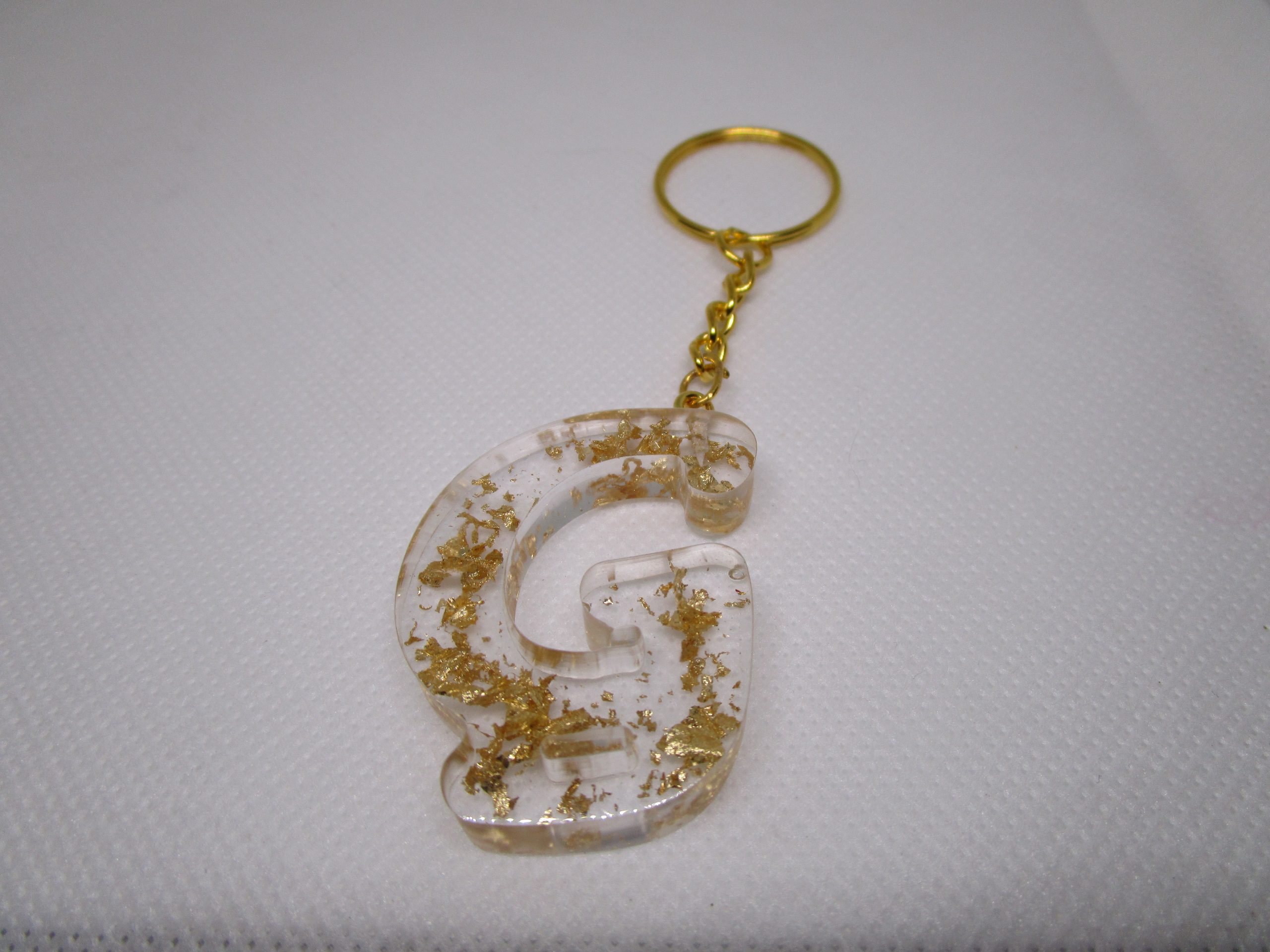 Porte-clés en résine transparente en forme de lettre "G", incrusté de feuilles d'or, avec un anneau doré et une chaîne.