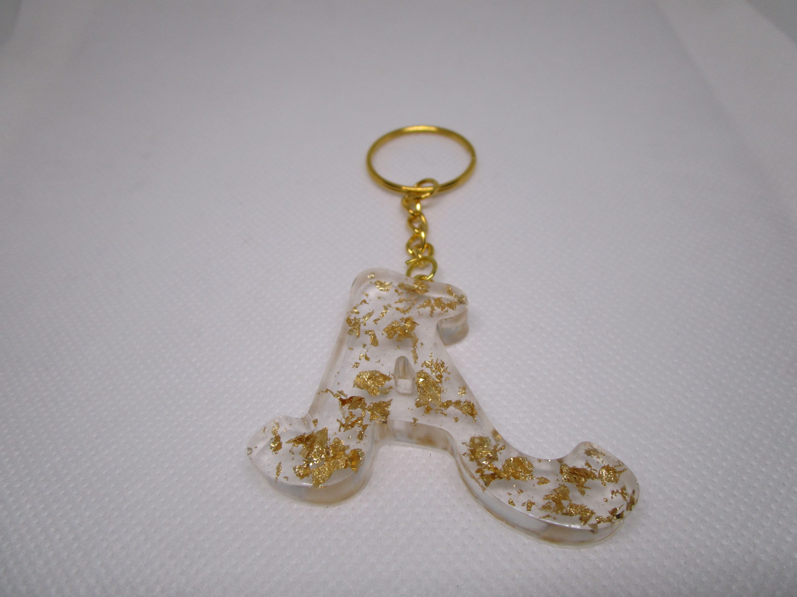 Porte-clés en résine transparente en forme de lettre "A", incrusté de feuilles d'or, avec un anneau doré et une chaîne.