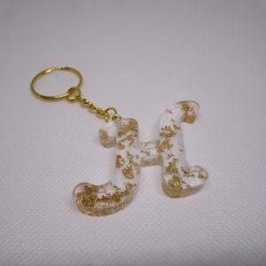 Porte-clés H : une lettre d'or capturée. La résine cristalline murmure des secrets. Des paillettes dorées dansent. Un bijou personnel, lumineux. Il chante votre initiale. Un éclat discret.