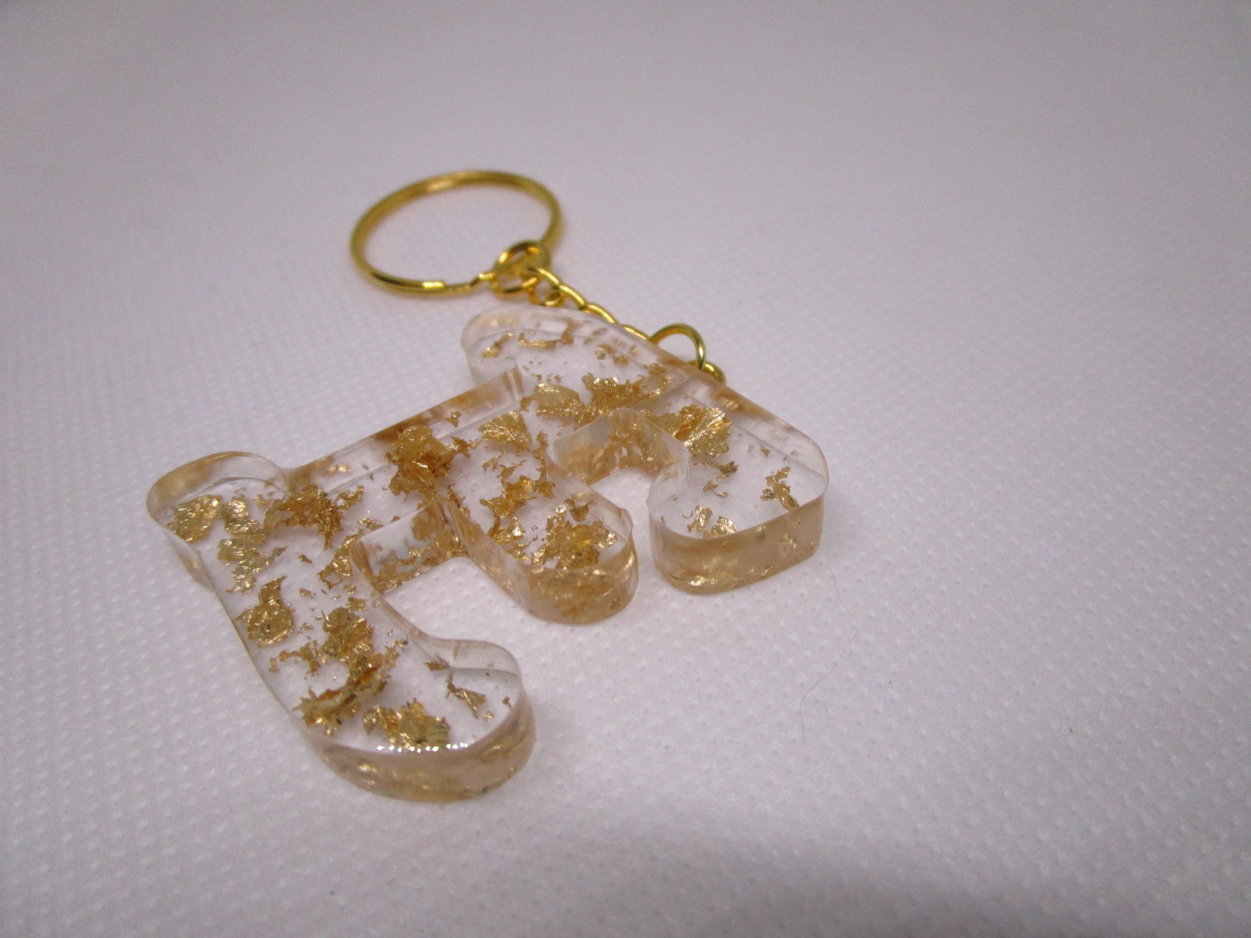 Porte-clés en résine transparente en forme de lettre "E", incrusté de feuilles d'or, avec un anneau doré et une chaîne.