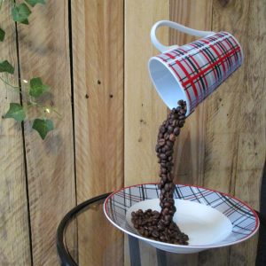 "Instant Figé". Sculpture artisanale Tasse écossaise rouge et grise. Grains de café bruns en suspension. Soucoupe blanche.