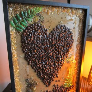 Love Cafée, Cadre décoratif unique Love Cafée en résine avec un cœur central formé de grains de café torréfiés, incrustations de feuilles d'or, de copeaux de bois, de petites feuilles de fougère et de mécanismes d'horlogerie steampunk.