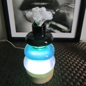 Vase lumineux décoratif fait main en résine empilée (bleu-vert et blanc) sur socle en bois clair, éclairé par LED (prise USB). Le col supérieur noir contient de fausses roses blanches.