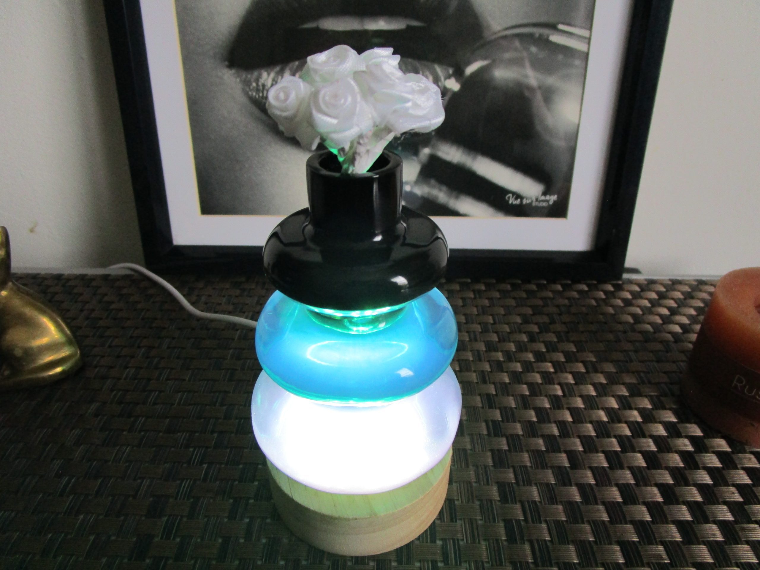 Vase lumineux décoratif fait main en résine empilée (bleu-vert et blanc) sur socle en bois clair, éclairé par LED (prise USB). Le col supérieur noir contient de fausses roses blanches.