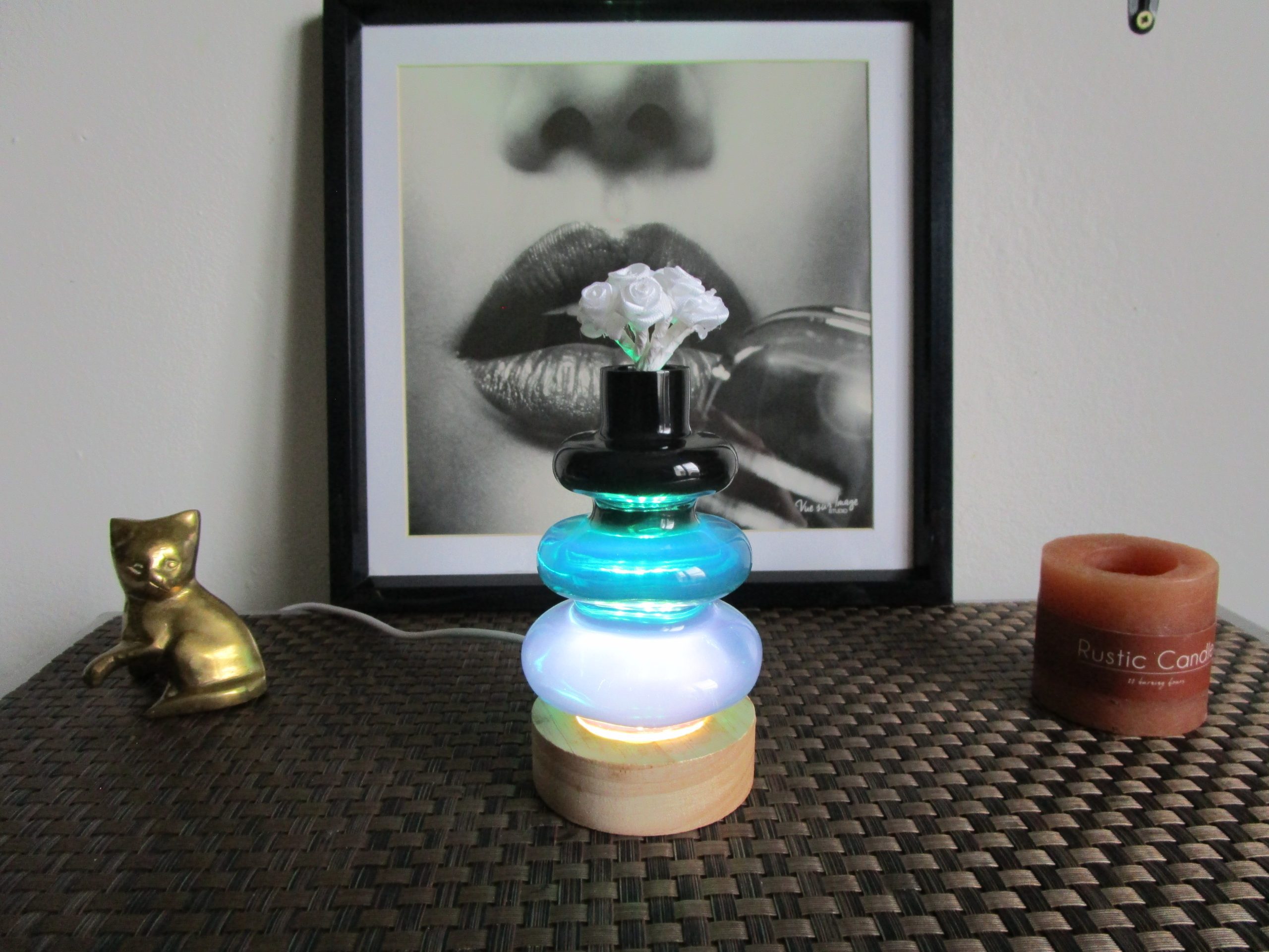 Vase lumineux décoratif fait main en résine empilée (bleu-vert et blanc) sur socle en bois clair, éclairé par LED (prise USB). Le col supérieur noir contient de fausses roses blanches.