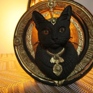 Magnet artisanal en résine représentant un buste de chat noir orné de bijoux argentés sur un disque jaune gravé de symboles.