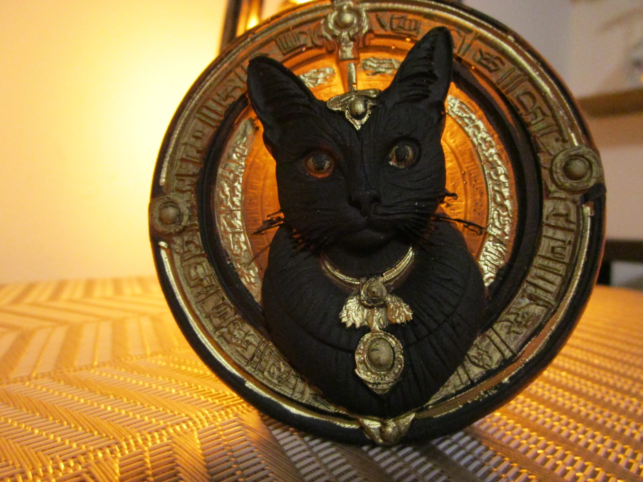 Magnet artisanal en résine représentant un buste de chat noir orné de bijoux argentés sur un disque jaune gravé de symboles.