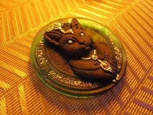 Magnet artisanal en résine représentant un chat noir orné de bijoux argentés sur un disque bleu translucide gravé de symboles ésotériques.