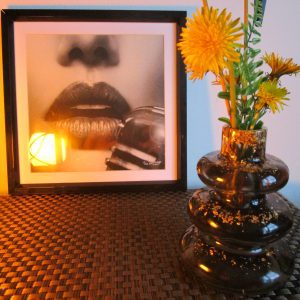 Vase artisanal en résine noire brillante avec inclusions de feuilles dorées, forme de galets empilés, fleurs jaunes en décoration.