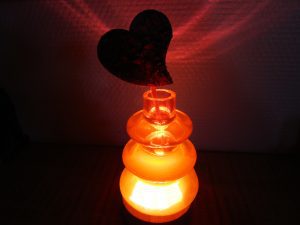 Vase artisanal en résine rouge lumineuse sur socle en bois avec un cœur en bois sculpté à l'intérieur.