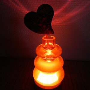 Vase artisanal en résine rouge lumineuse sur socle en bois avec un cœur en bois sculpté à l'intérieur.