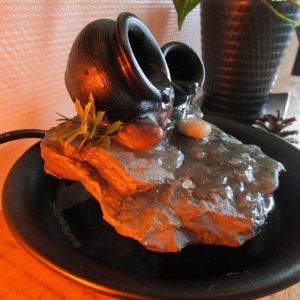 Fontaine d'intérieur artisanale noire nommée Le Murmure des Jarres, composée de deux petites jarres sur une pierre avec un écoulement d'eau lumineux.